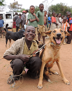 A happy boy holds his dog on a leash while other boys look on.